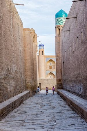 KHIVA, UZBEKISTAN - SEPTEMBER 7: Three kids walking in the street between high walls of Khiva old town. September 2016のeditorial素材