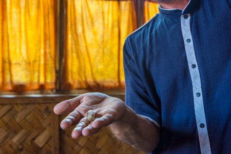 Man showing silk thread coming from a silk worm cocoon in a silk factoryの写真素材