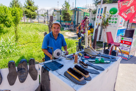 MARGILAN, UZBEKISTAN - AUGUST 20: Shoemaker with basic tools to repair and clean the shoes at the...