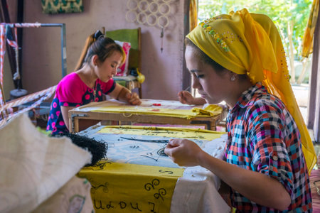 MARGILAN, UZBEKISTAN - AUGUST 20: Woman embroidering fabric by hand with traditional Uzbek patterns in a silk factory workshop. August 2016のeditorial素材