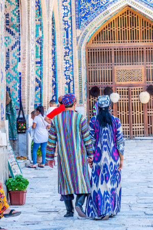 SAMARKAND, UZBEKISTAN - AUGUST 28: Couple dressed up in traditional Uzbek wedding clothes - colorful and patterns from the back in Samarkand Registan. August 2016のeditorial素材