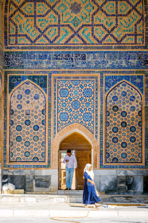 SAMARKAND, UZBEKISTAN - Woman and man in front of colorful wall of blue mosaic in Samarkand, Registan, Uzbekistan. August 2016のeditorial素材