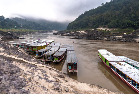 Long boats for a ride down the river Mekong at river bank in late afternoon sun, Mekong river, Laosの写真素材
