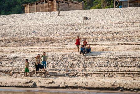 Mekong river, Laos - Feb 2016: Group of kids sitting and greeting from the river bank of Mekong riverのeditorial素材