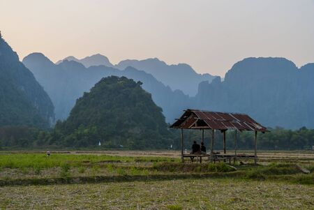 Vang Vieng, Laos - Feb 2016: Group of friends sitting in a hutt and observing beautiful sunset in mountains surrounding Vang Viengの写真素材