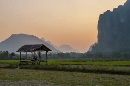 Vang Vieng, Laos - Feb 2016: Group of friends sitting in a hutt and observing beautiful sunset in mountains surrounding Vang Viengの写真素材