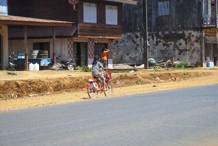 Pakse, Laos - Feb 2016: Girl riding a bike along the road in village in Laosの写真素材