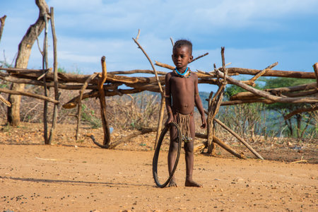 Turmi, Ethiopia - Nov 2018: Hamer tribe kid playing with the tire. Tire is a common toy in the...
