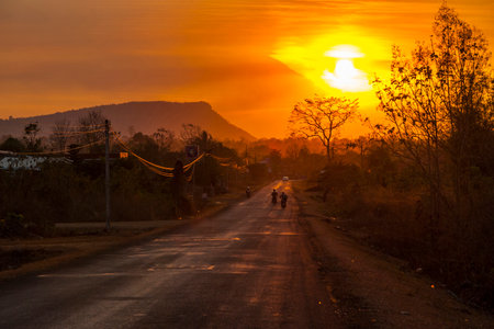 Motorbike silhouette driving on a scenic road in orange sunset in countryside of Laosのeditorial素材