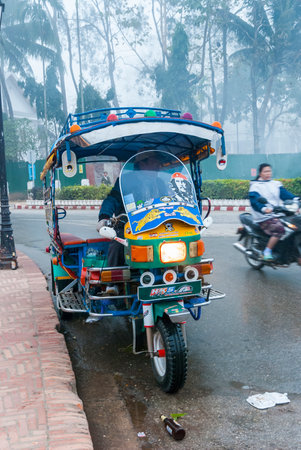Luang Prabang, Laos - Feb 2016: Colorful tuk tuk and driver waiting by the road in early morning, Luang Prabang, Laosのeditorial素材