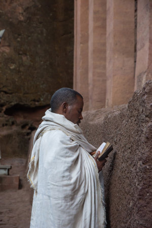 Lalibela, Ethiopia - Nov 2018: Man dressed up in white traditional ethiopian clothes praying at the rock excavated church in Lalibela.のeditorial素材