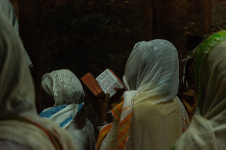 Lalibela, Ethiopia - Nov 2018: Women dressed up traditional white, sitting in twilight and reading prayers book next to the underground churches of Lalibelaのeditorial素材