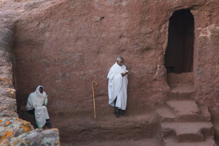 Lalibela, Ethiopia - Nov 2018: People dressed up in white traditional ethiopian clothes praying next to church excavated in rock in Lalibela.のeditorial素材