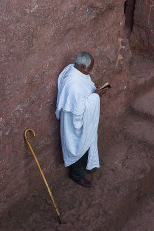 Lalibela, Ethiopia - Nov 2018: People dressed up in white traditional ethiopian clothes praying next to church excavated in rock in Lalibela.のeditorial素材