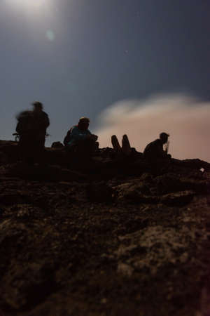 Silhouettes of people sitting at the edge of Erta Ale volcano crater, Ethiopia, in full moonの写真素材