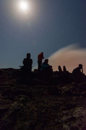 Silhouettes of people sitting at the edge of Erta Ale volcano crater, Ethiopia, in full moonの写真素材