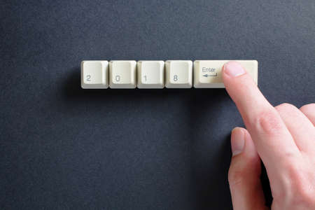 index finger of a mans hand presses on the keyboard, on which is written 2018 and enter ket on a black background. New year 2018 card.の写真素材