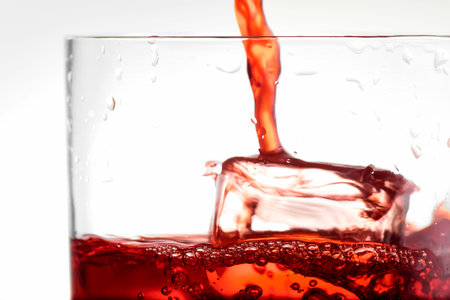 Red drink falling into a glass with ice in close up