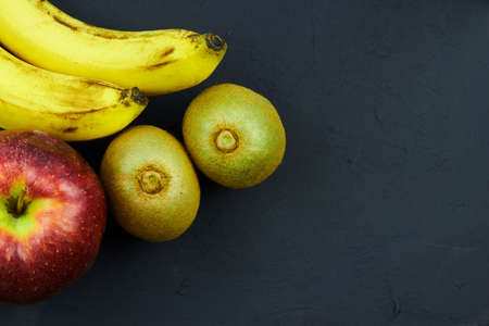 Composition of yellow banana, red apple and green kiwi on a dark backgroundの写真素材