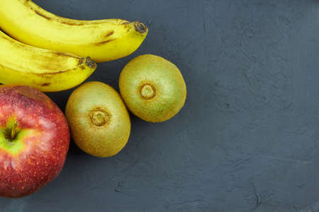 Still life with fruit. Close up view of red apples, bananas and kiwi on dark background with copy space for textの写真素材