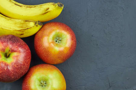 Fresh fruits. Top view of red apples and bananas on dark background with copy space for text.の写真素材