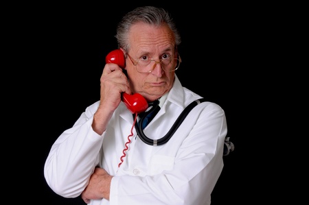 Senior doctor wearing a stethoscope isolated on black and talking on a telephoneの写真素材