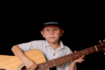 Young boy wearing a cowboy hat isolated on black playing the guitar