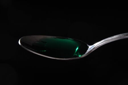 Green liquid medicine on a spoon isolated on blackの写真素材