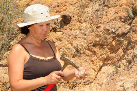 Senior woman geologist tap a rock formation with a hammerの写真素材