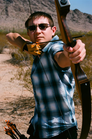 Young man shooting a bow and arrow in the desert