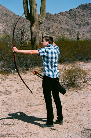 Young man shooting a bow and arrow in the desertの写真素材