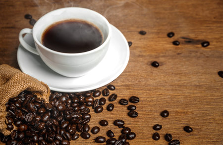 A cup of coffee that have smoke and beans on wooden table. espresso can use for diet plan.