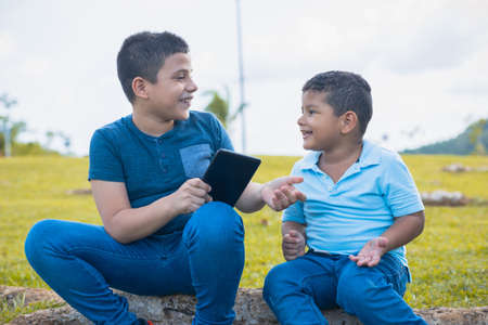Latino brothers talking while looking at the cell phone sitting on the treeの写真素材