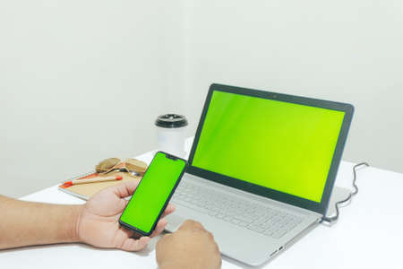 person checking mobile while working on laptopの写真素材