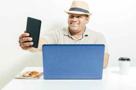 Hispanic man taking a self-portrait with his cell phone while working on his laptop on the desk