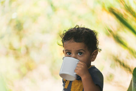 latin boy drinking coffee in a white cup, in a natural environmentの写真素材