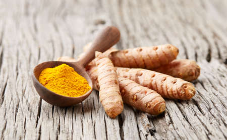 Turmeric roots with curry powder on old wooden backgroudの写真素材