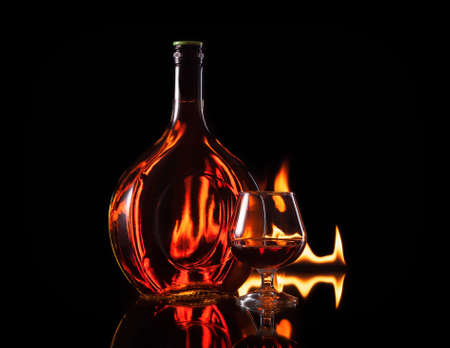 Bottle glass of cognac in fire flame on black backgroundの写真素材