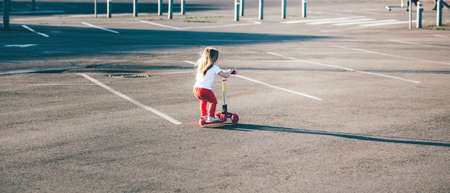Little beautiful girl riding a scooter at sunsetの写真素材