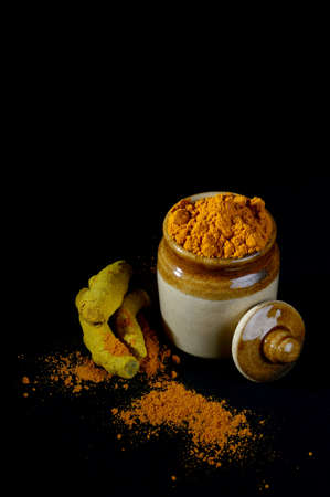 Turmeric powder in clay pot with roots or barks on black backgroundの写真素材