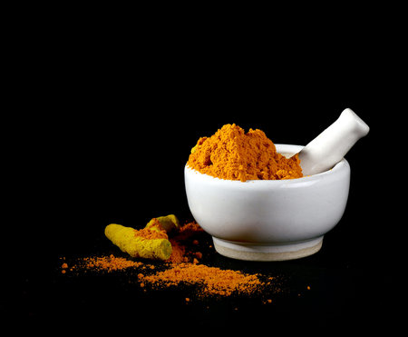 Turmeric powder in mortar with pestle and roots or barks on black backgroundの写真素材