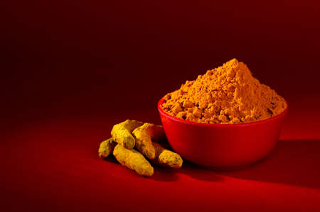 Dry Turmeric powder and roots or barks in red bowl on red backgroundの写真素材