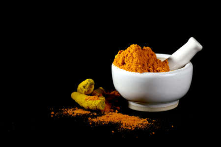 Turmeric powder in mortar with pestle and roots or barks on black backgroundの写真素材
