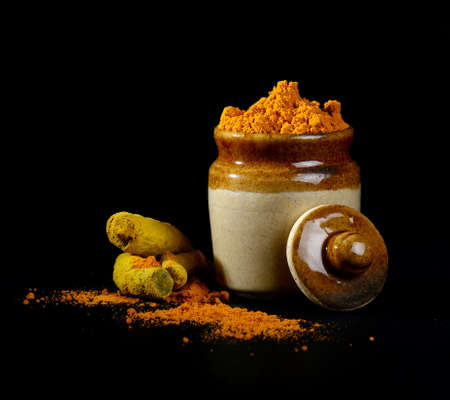 Turmeric powder in clay pot with roots or barks on black backgroundの写真素材