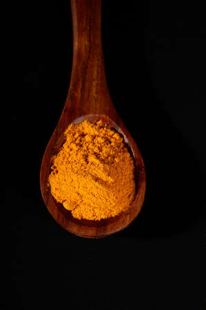 Turmeric powder in spoon on black backgroundの写真素材