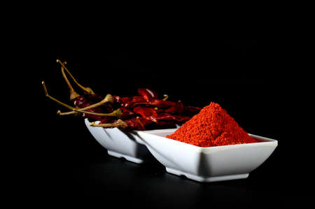 chilly powder with red chilly in white plate, dried chillies on black backgroundの写真素材
