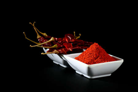 chilly powder with red chilly in white plate, dried chillies on black backgroundの写真素材
