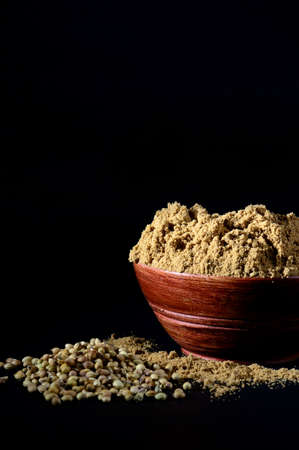 Coriander Powder in wooden bowl with seeds on black backgroundの写真素材