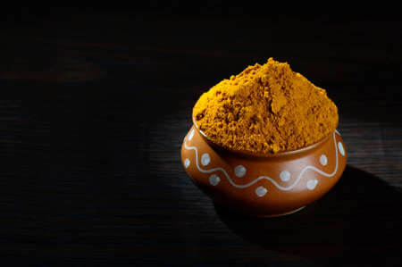 Turmeric powder in clay pot with roots or barks on black backgroundの写真素材