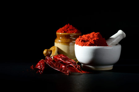 Red Chili Pepper powder in pestle with mortar and clay pot with Red Chili Peppers on black...